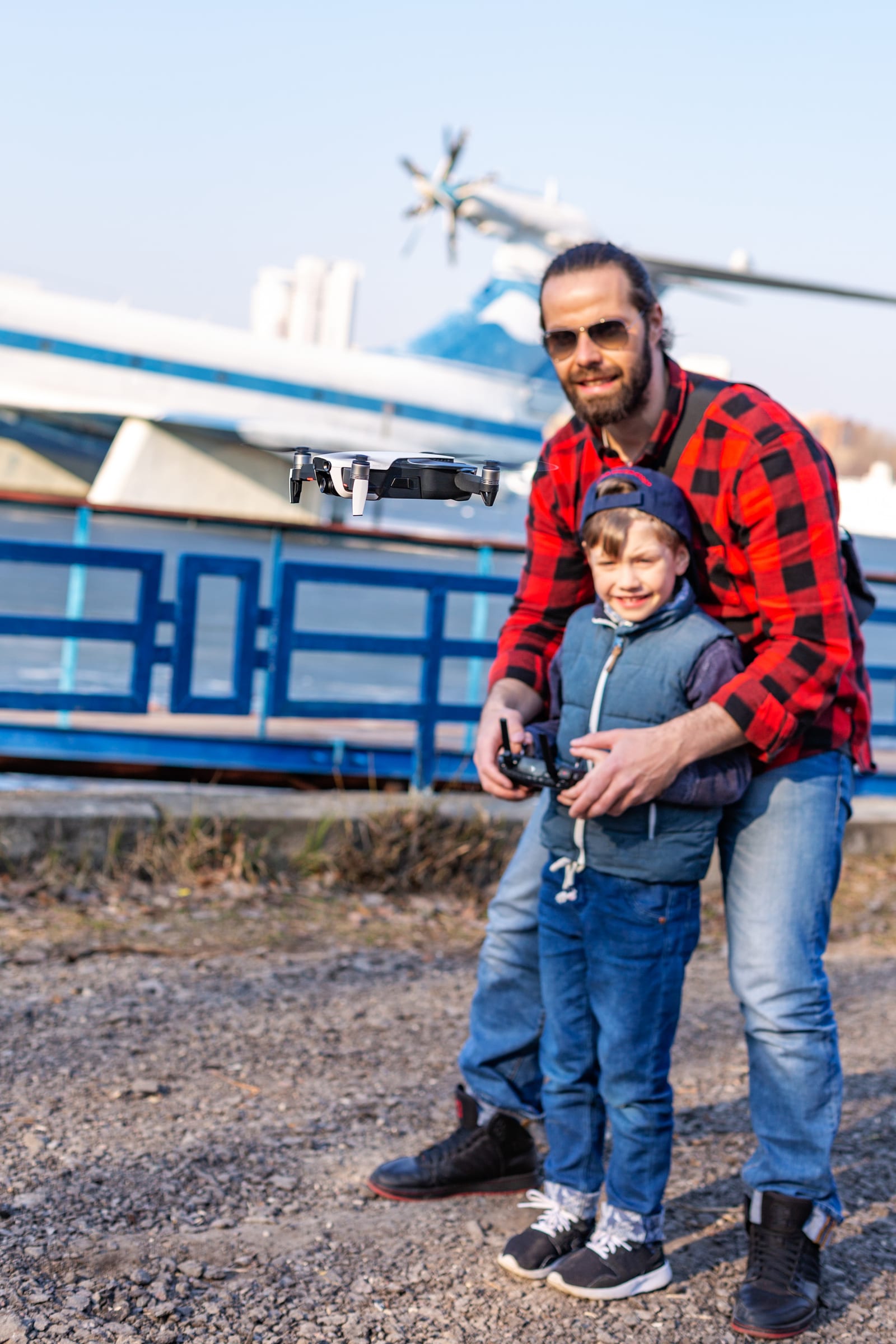 Pai e filho pilotando um pequeno quadricóptero à beira de um rio