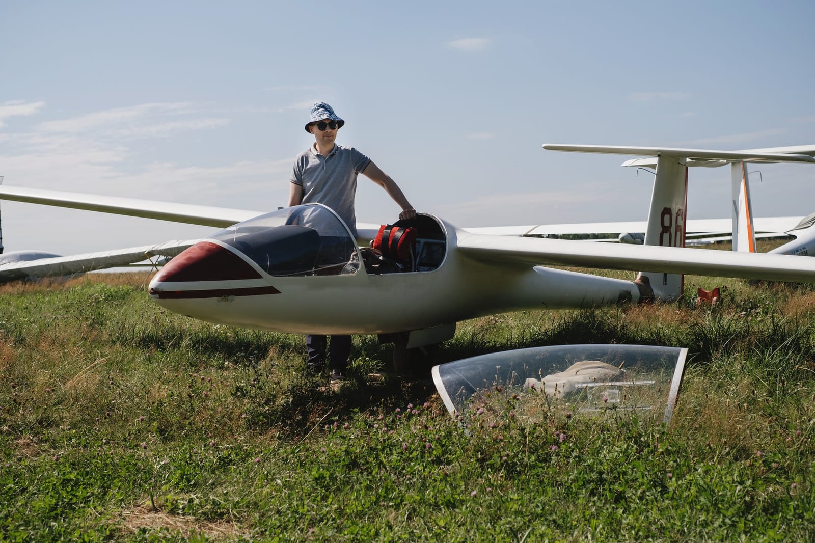 Piloto ao lado de um planador branco estacionado num campo de grama